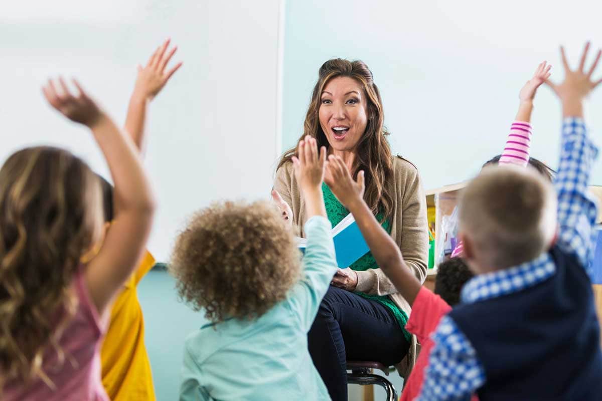 preschool teacher children raising hands in class